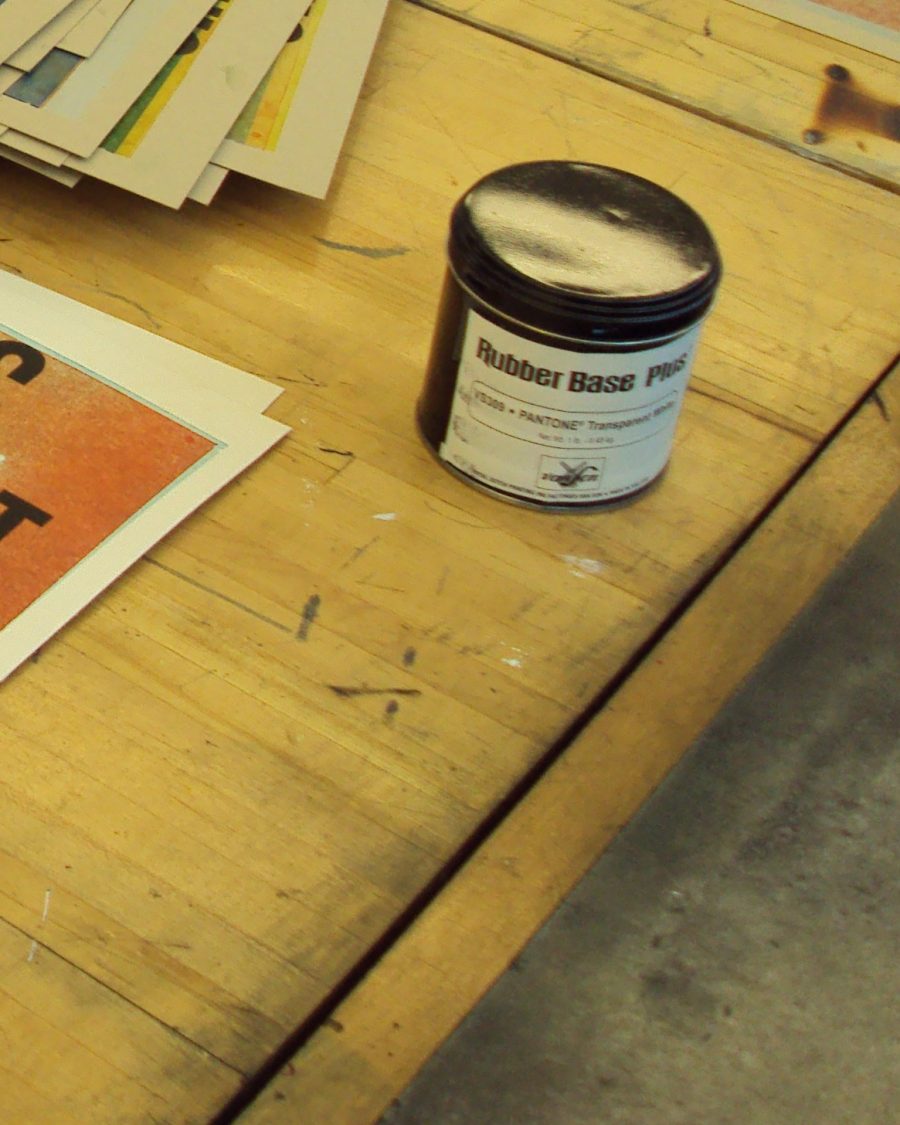 Pantone-matched letterpress ink can on a press bed beside proof sheets