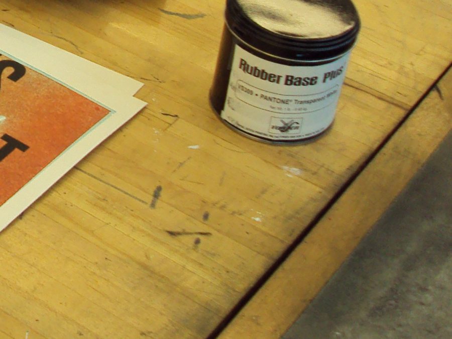Pantone-matched letterpress ink can on a press bed beside proof sheets